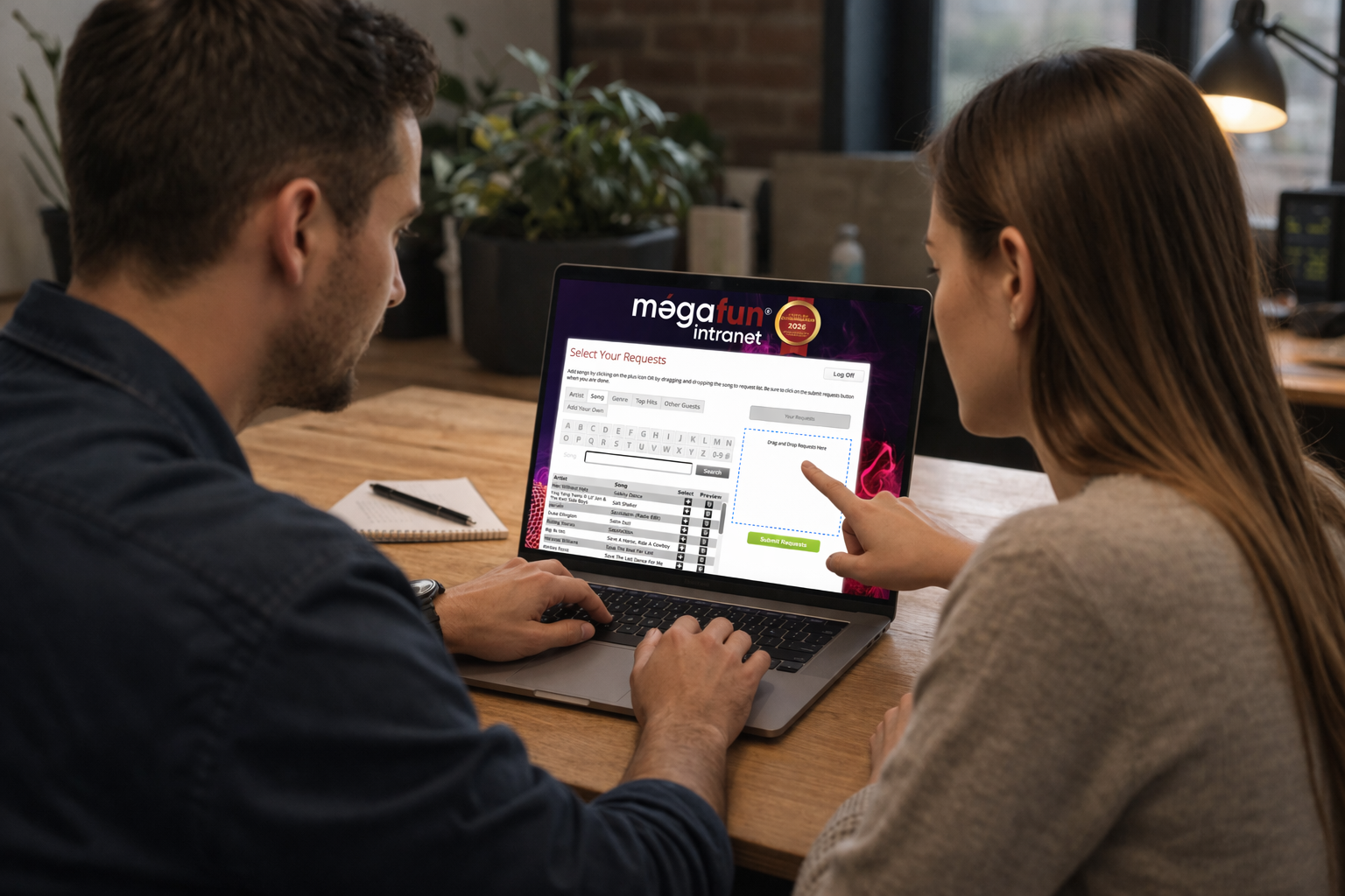 Couple assis devant un ordinateur portable utilisant l’intranet Mégafun pour sélectionner des chansons via une interface de demande musicale, dans un environnement chaleureux et moderne.